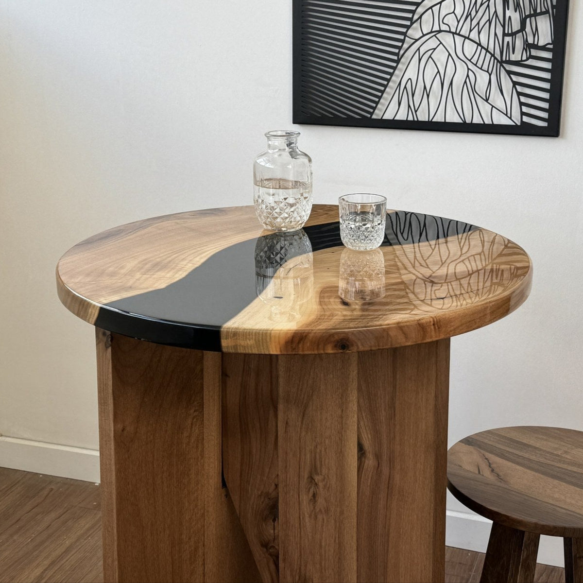 Close-up of the round walnut bar table's black epoxy river top and its slab base