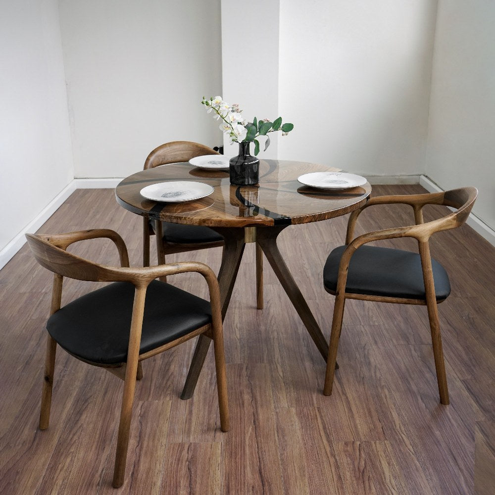 Round walnut dining table with epoxy swirl and wooden tripod base in a white room with two armchairs