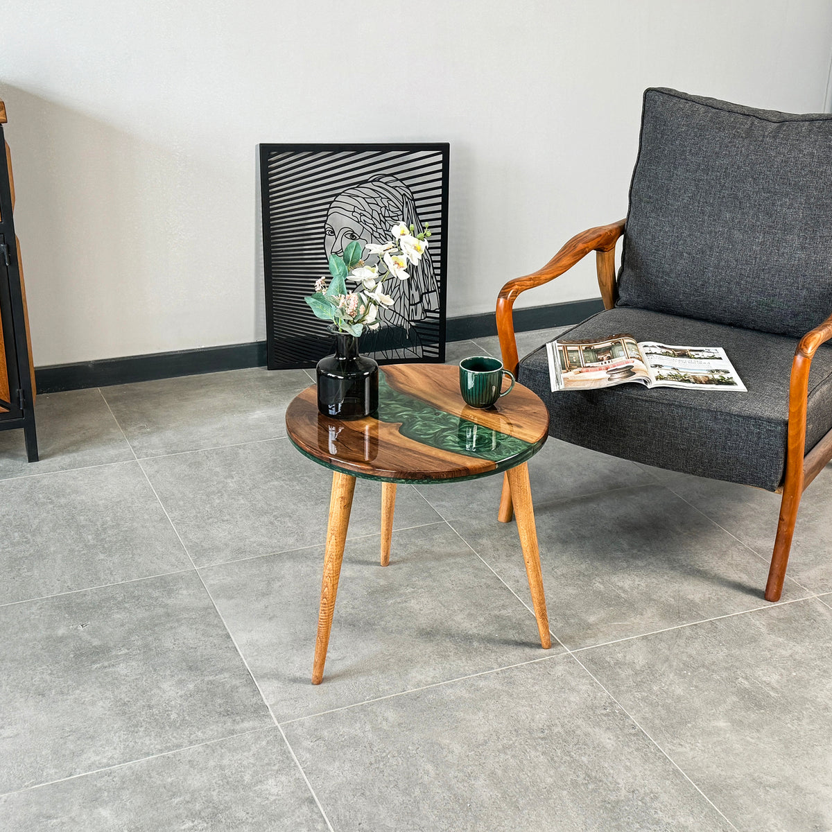 Green epoxy river round side table beside a gray armchair on a tile floor, wide view