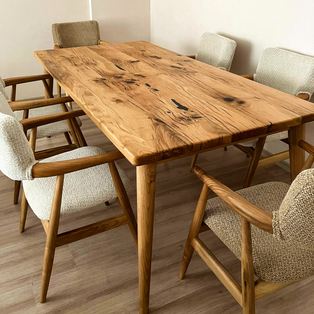 Solid oak dining table with tapered legs and gray armchairs, viewed from a corner