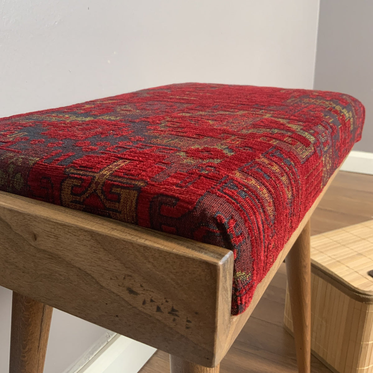 Close-up of the red patterned seat cushion and the wooden frame edge of the keyboard bench