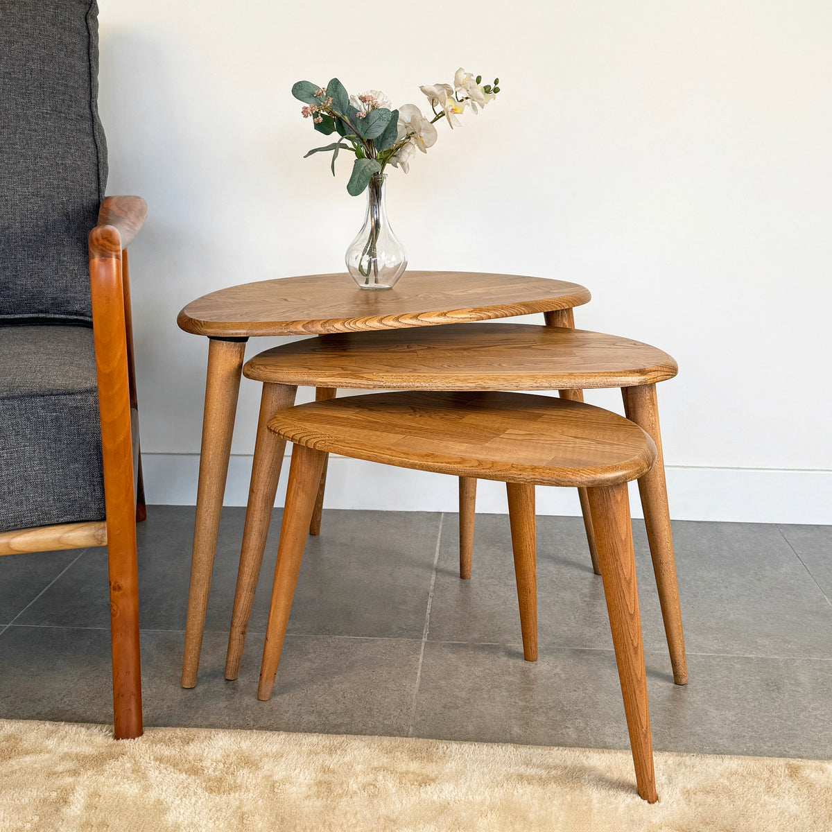 Natural-Chestnut Ercol style nesting table set of 3 on a gray tile floor in front of an armchair