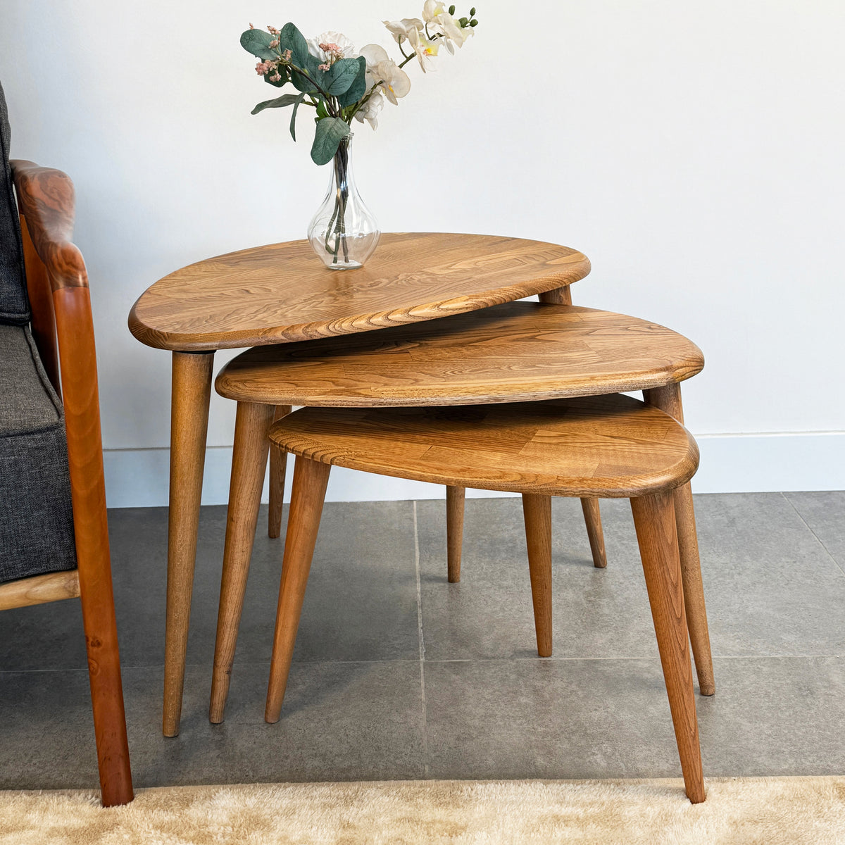 Natural-Chestnut chestnut nesting tables seen from a higher angle next to a gray armchair