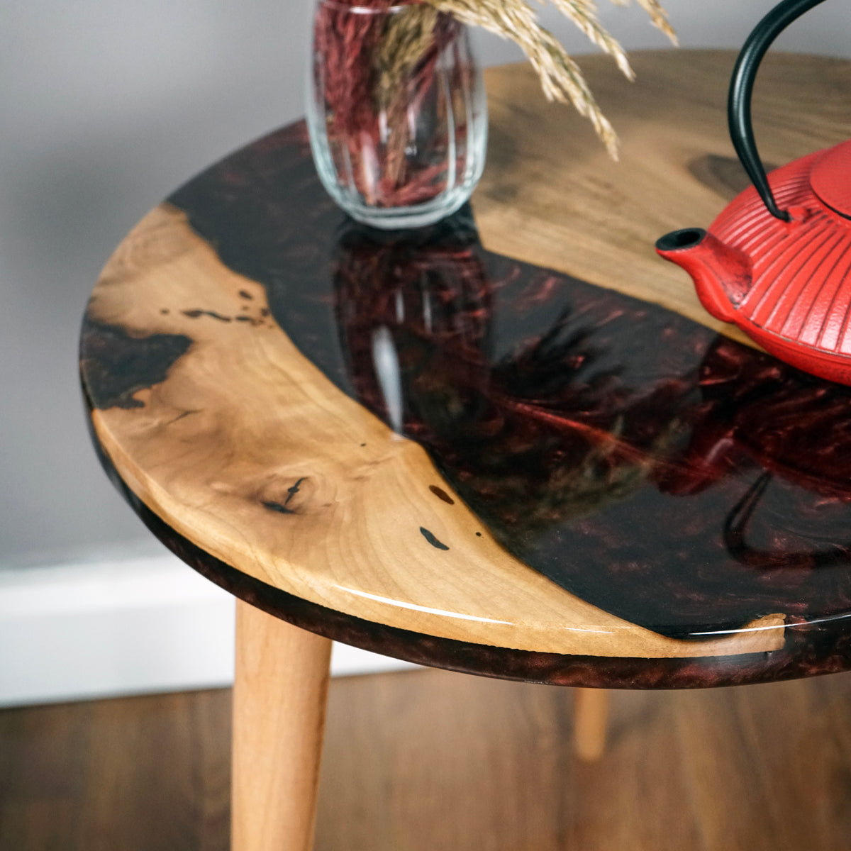 Close-up of the maroon epoxy river and live edge walnut on the round side table top with a red teapot
