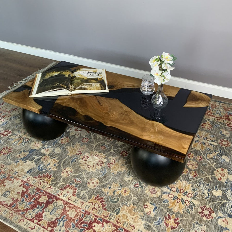 Black epoxy river walnut coffee table on black ball legs, angled view from the long side with an open book