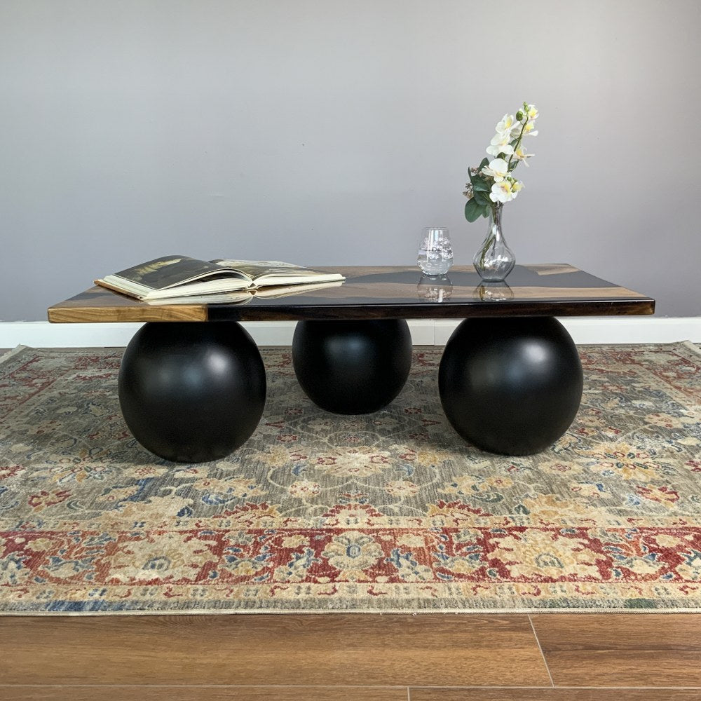 Straight front view of the walnut coffee table with black epoxy top and three black ball legs