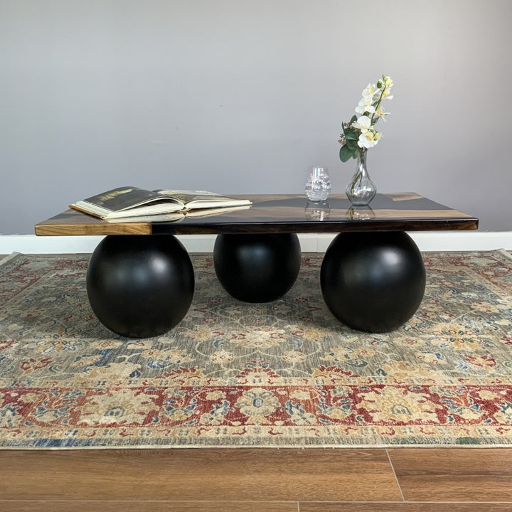 Straight front view of the walnut coffee table with black epoxy top and three black ball legs