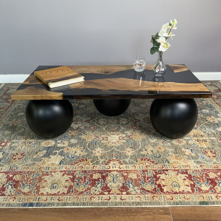 Low front view of the walnut and black epoxy coffee table resting on three black ball legs