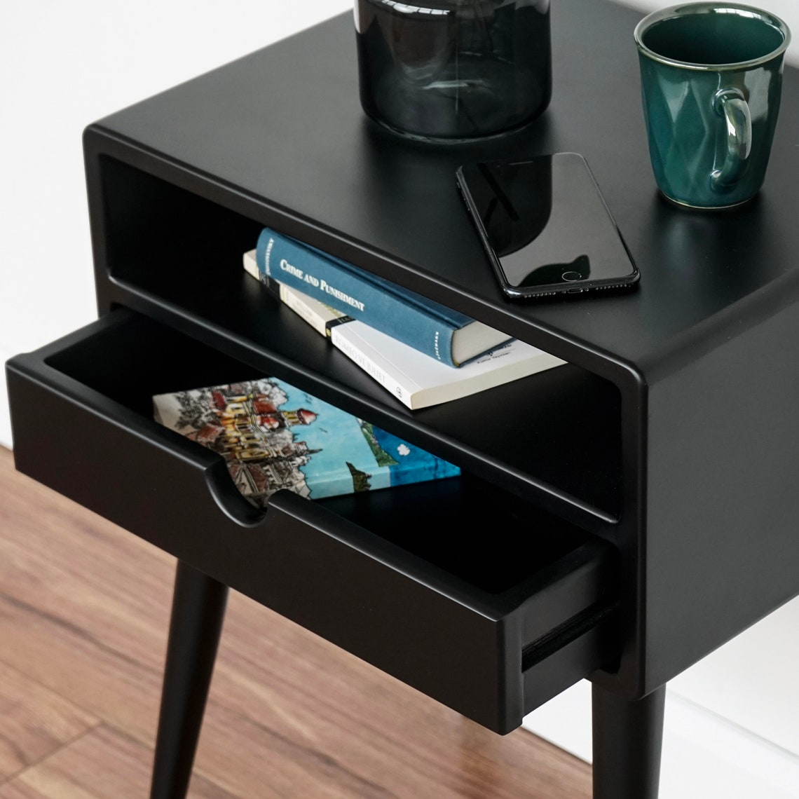 Close-up of the black nightstand drawer pulled open below the open shelf, with a magazine inside