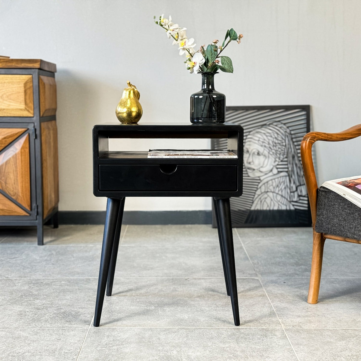 Front view of the black MDF side table with open shelf, one drawer and tapered legs