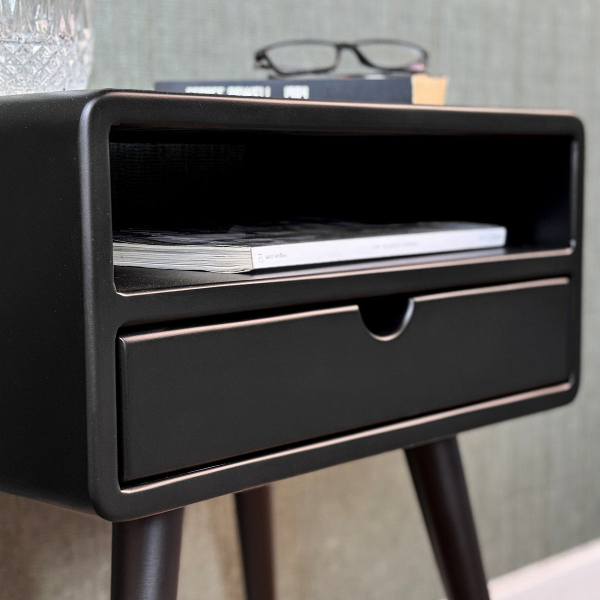 Close-up of the rounded corner, open shelf and drawer front of the black mid century side table