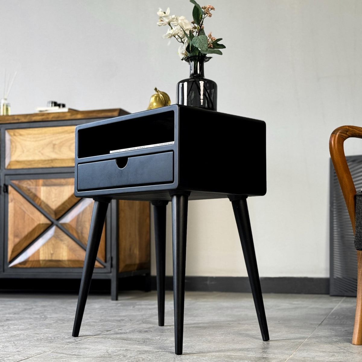 Low angle on the black mid century side table from the side, showing the drawer and tapered legs