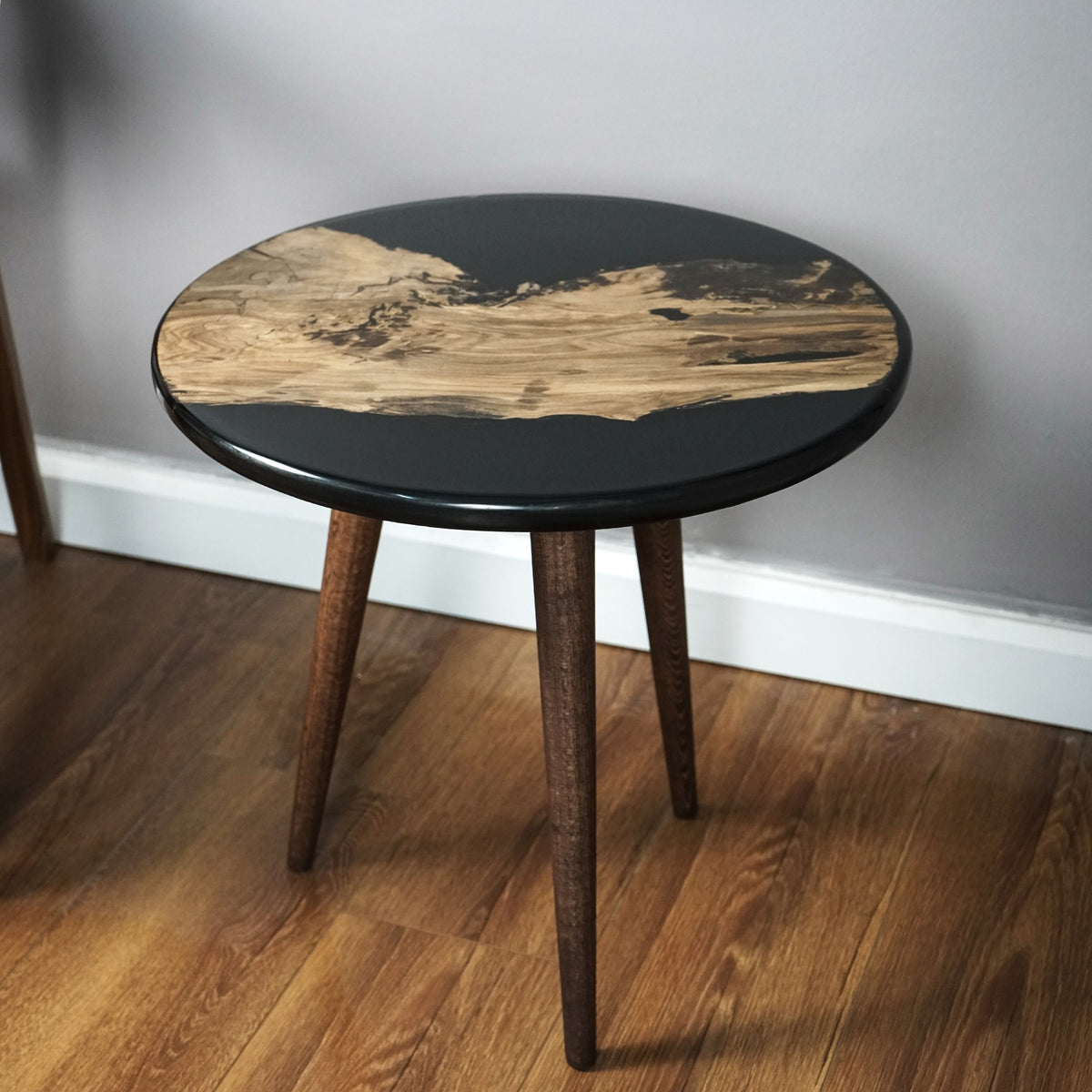 Black walnut epoxy side table with dark tapered legs, front angle against a gray wall