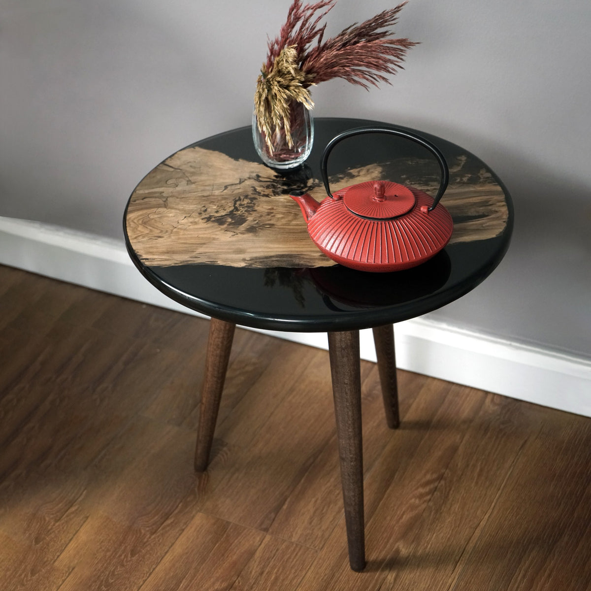 Round black epoxy side table with a walnut island on top and tapered legs, in a room corner