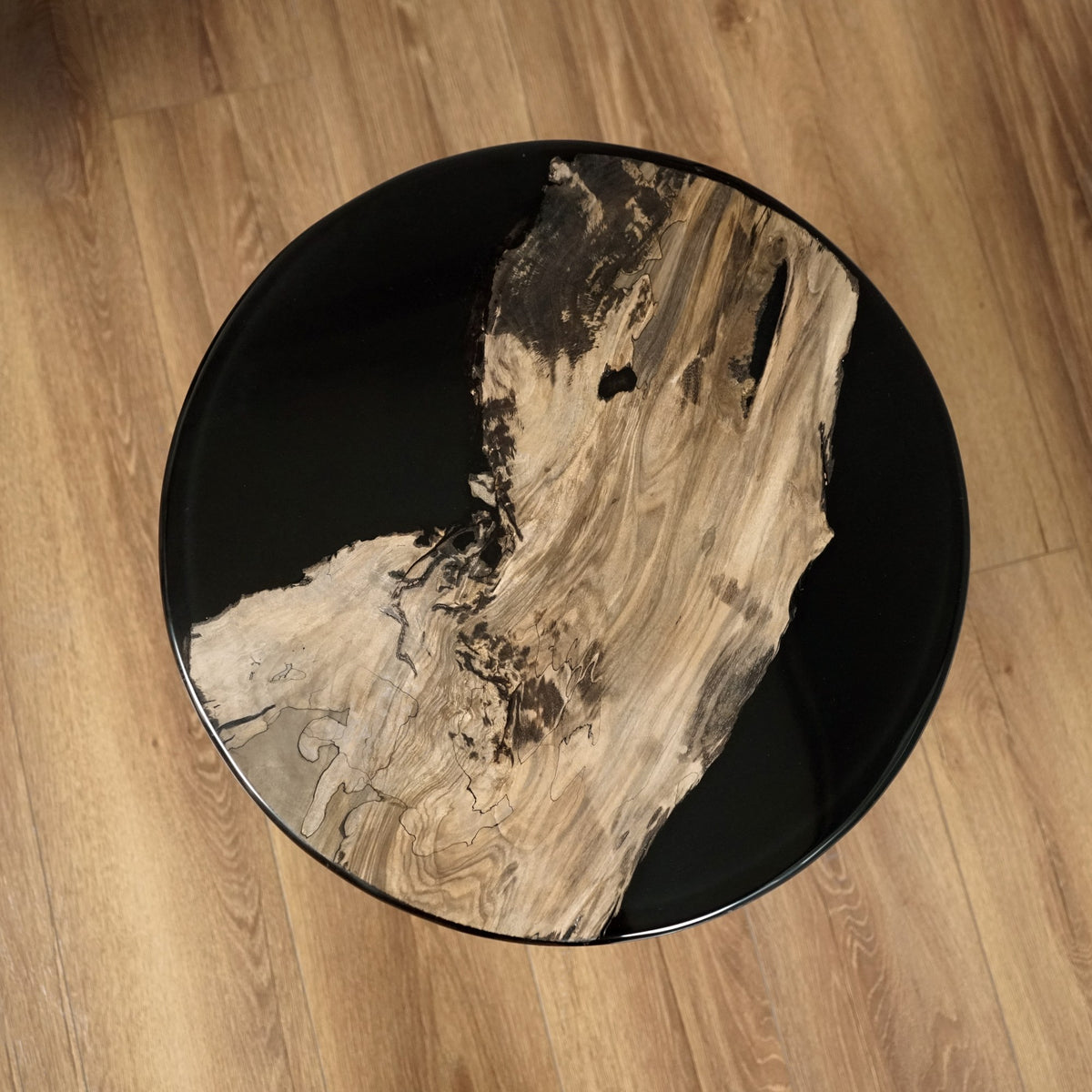 Top-down view of the round side table with a walnut slab set in glossy black epoxy resin on a wood floor
