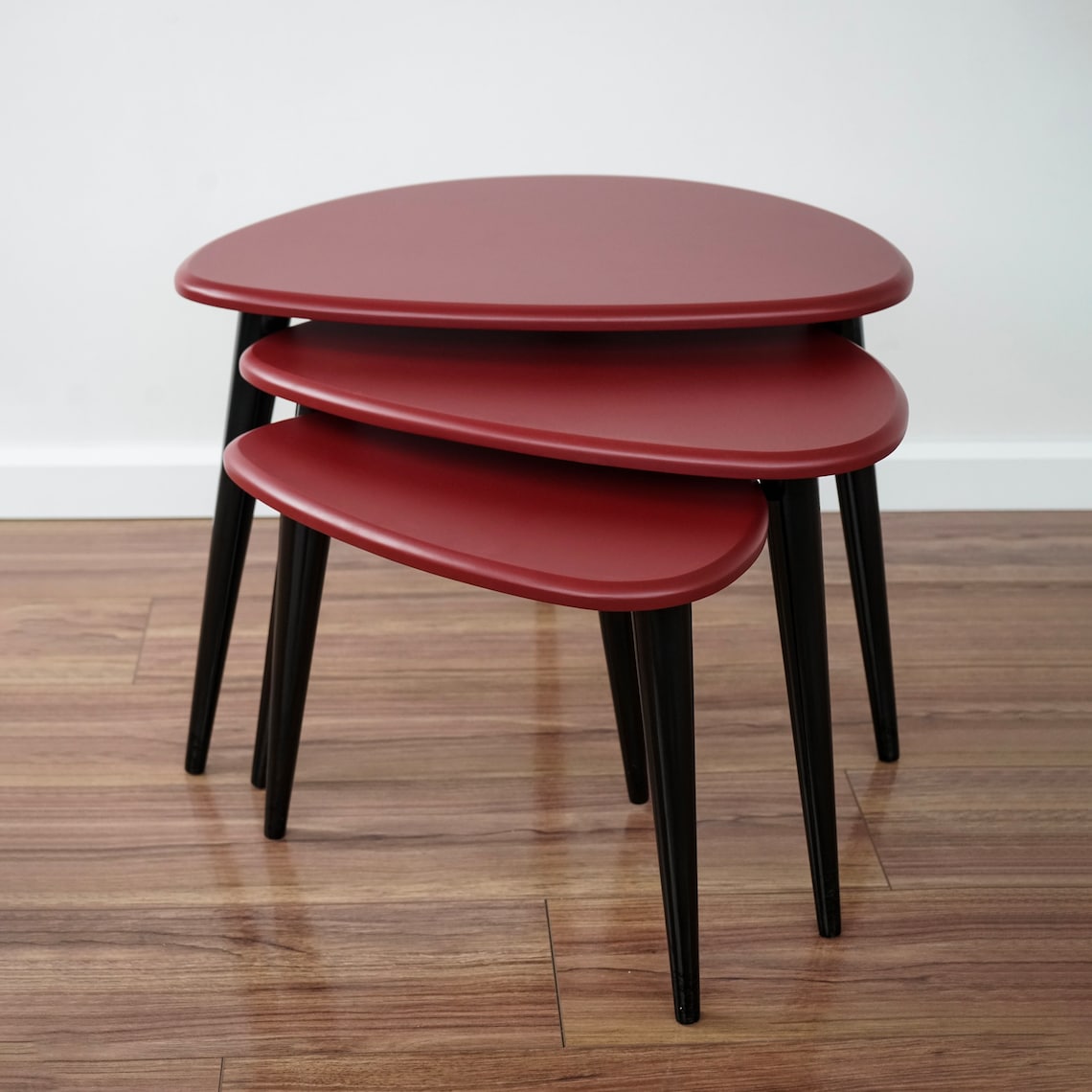 Set of three burgundy pebble nesting tables with black legs, bare tops on a wood floor