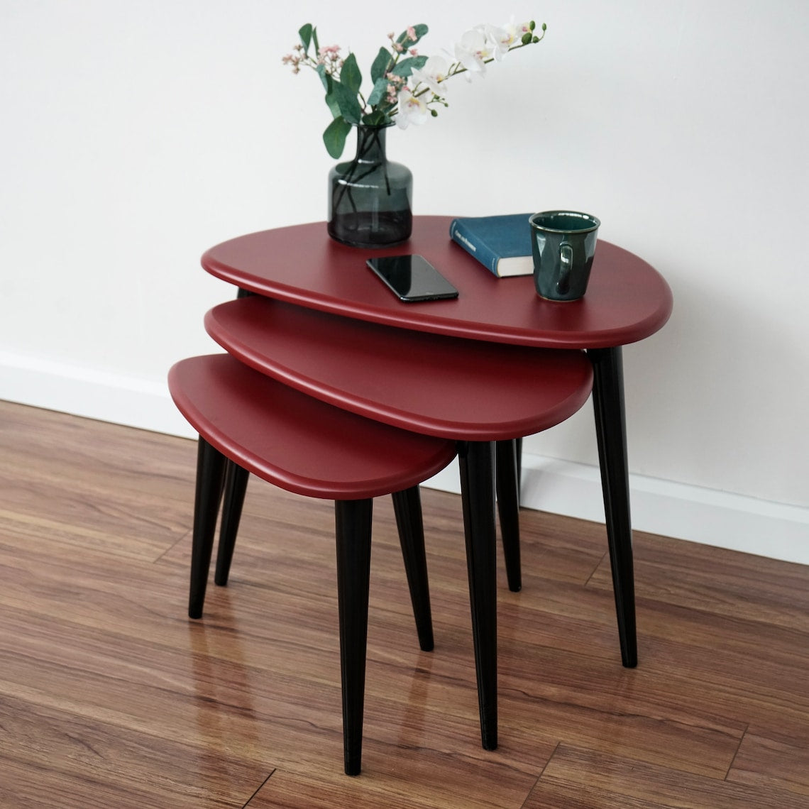 Corner view of the burgundy nesting tables set of 3, tops stacked at graduated heights