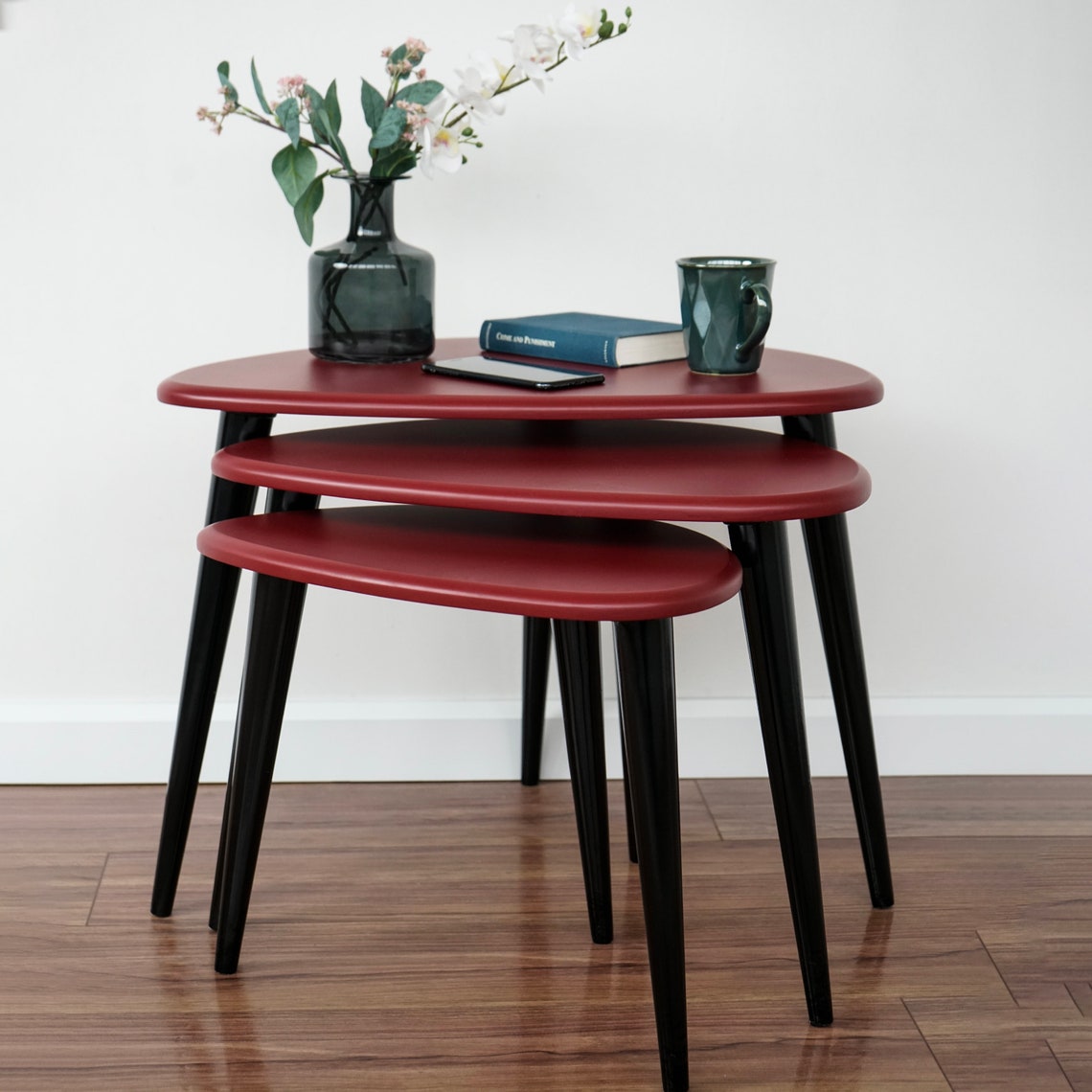 Low front view of the burgundy pebble nesting tables with a vase of flowers on the top table