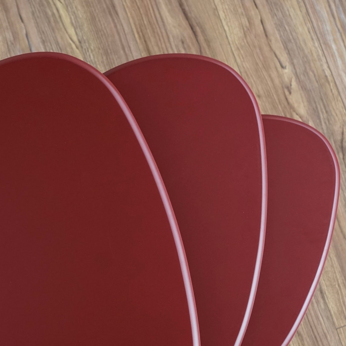 Overhead close-up of the three burgundy pebble table tops fanned out above a wood floor
