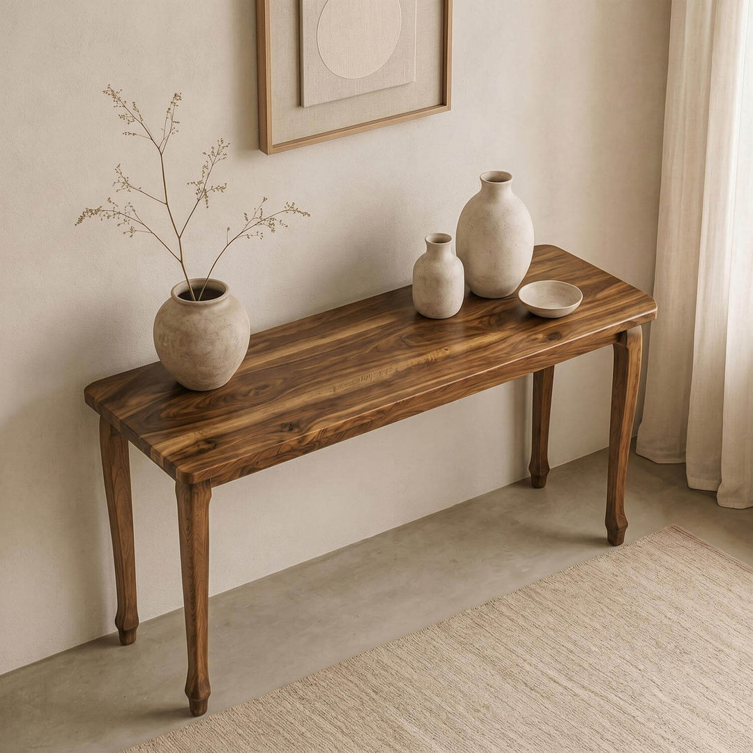 Cabriole legged walnut console table positioned against a neutral wall, decorated with rustic earthenware and dried branches.