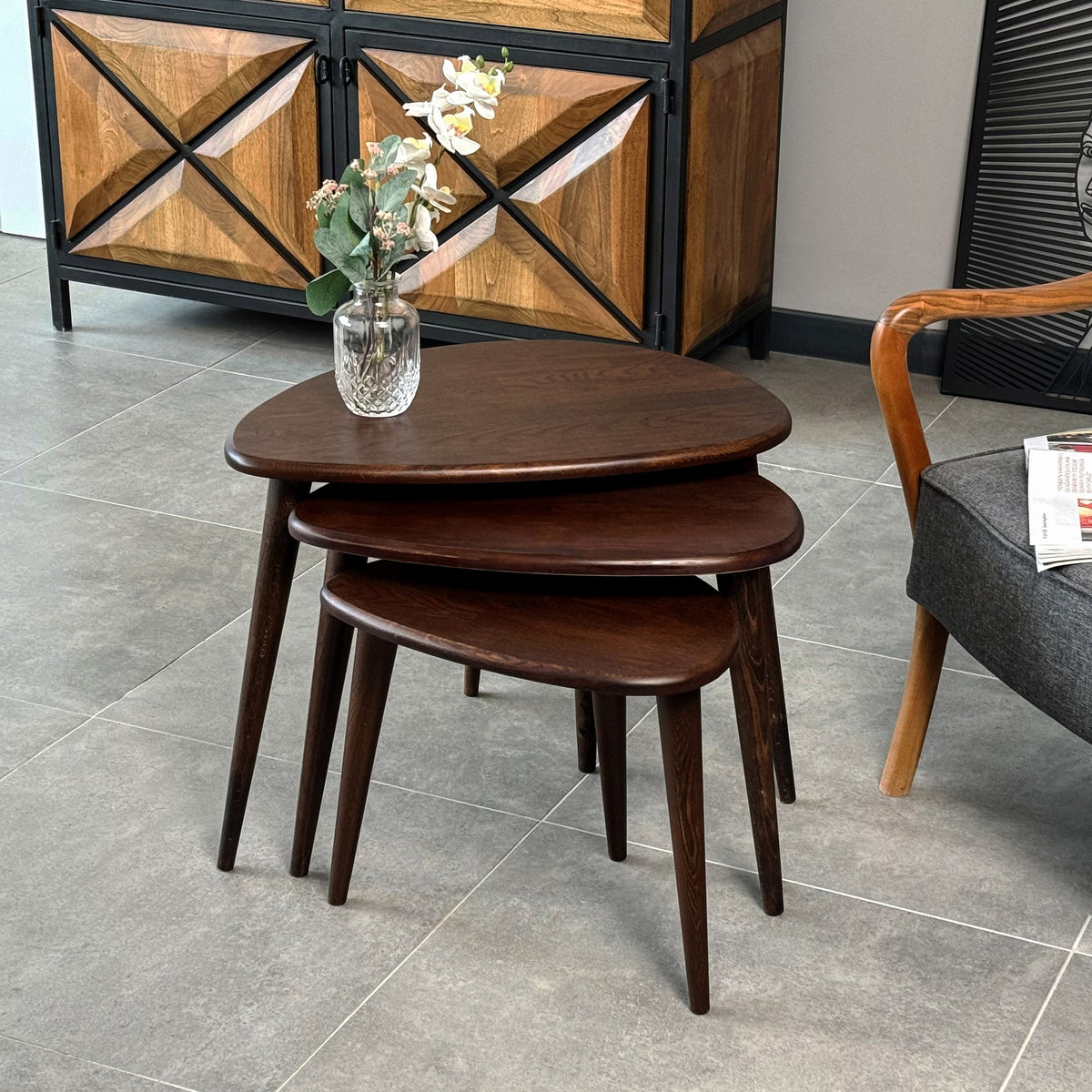 Chocolate oak nest of tables, closer view with a glass vase and a cabinet behind