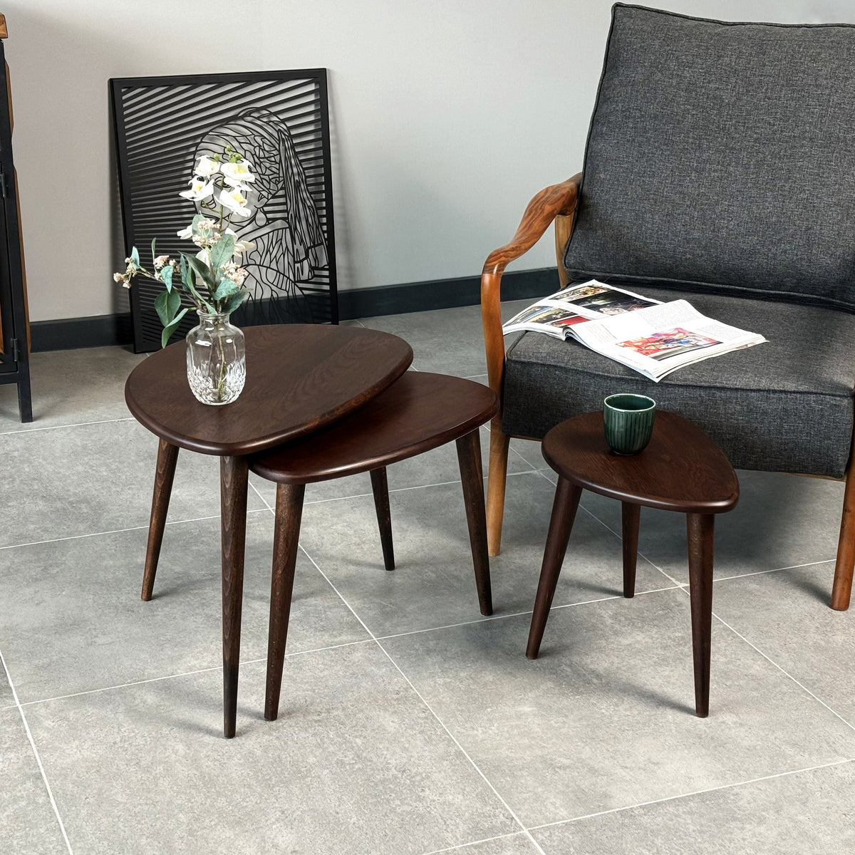 Chocolate oak nest of tables with the small table separated, next to a gray armchair