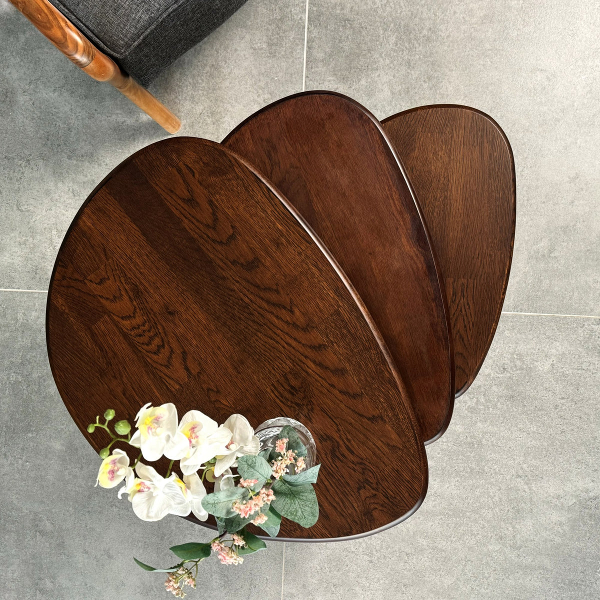 Top view of three chocolate oak nesting table tops fanned out, with flowers at the edge