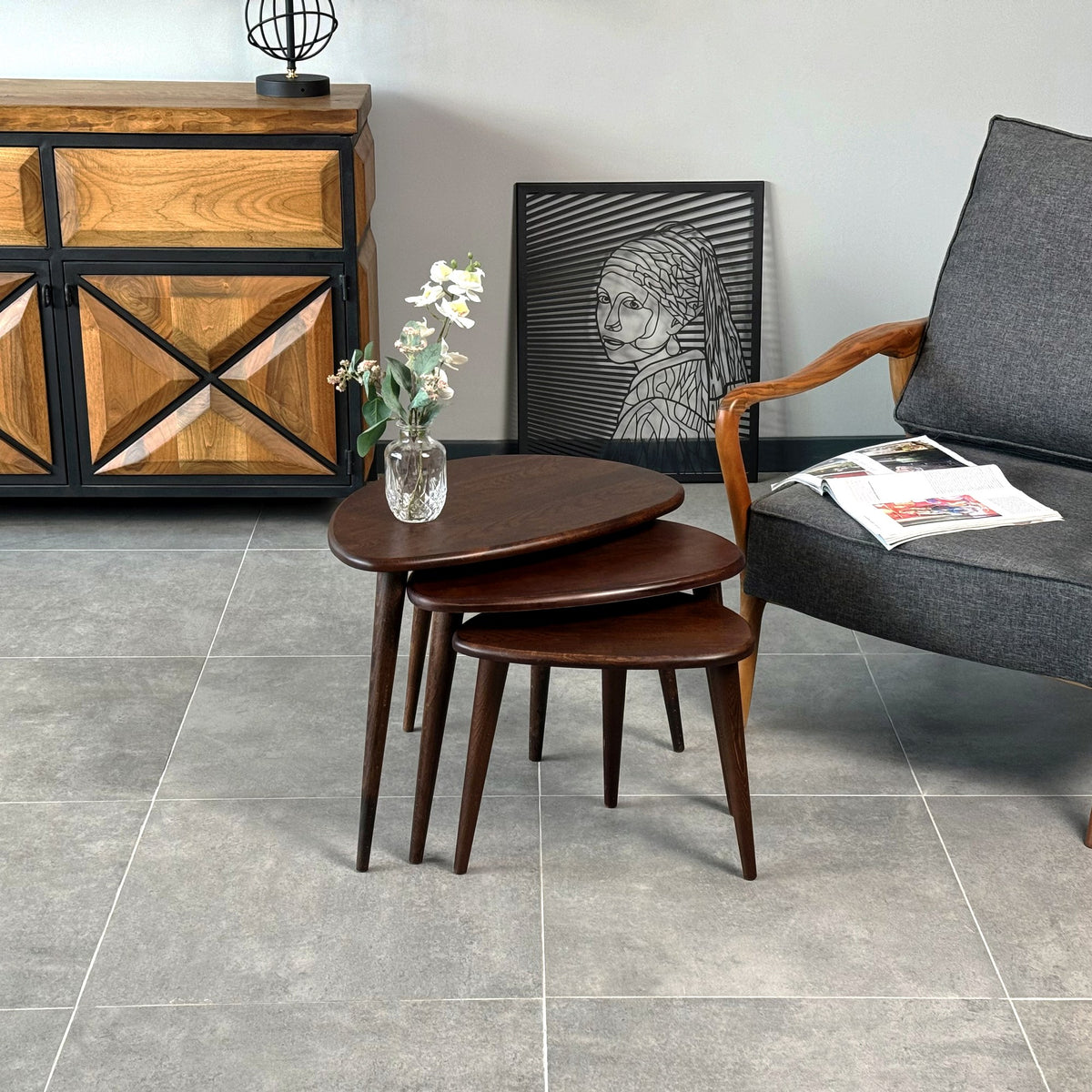 Chocolate oak Ercol style nesting tables in front of a wooden cabinet with an X pattern
