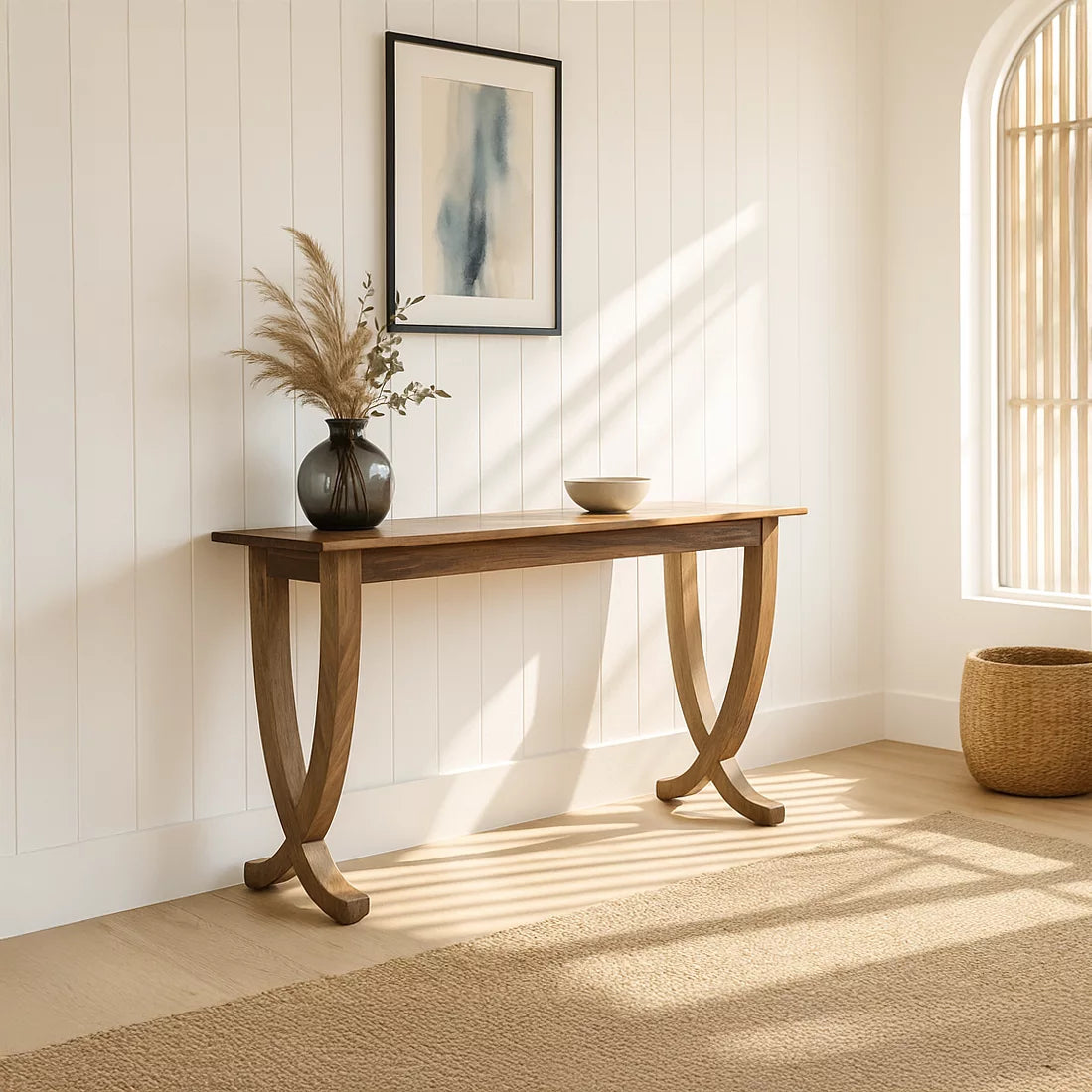 Walnut console table with curved legs on a white paneled wall beside an arched window with sunlight