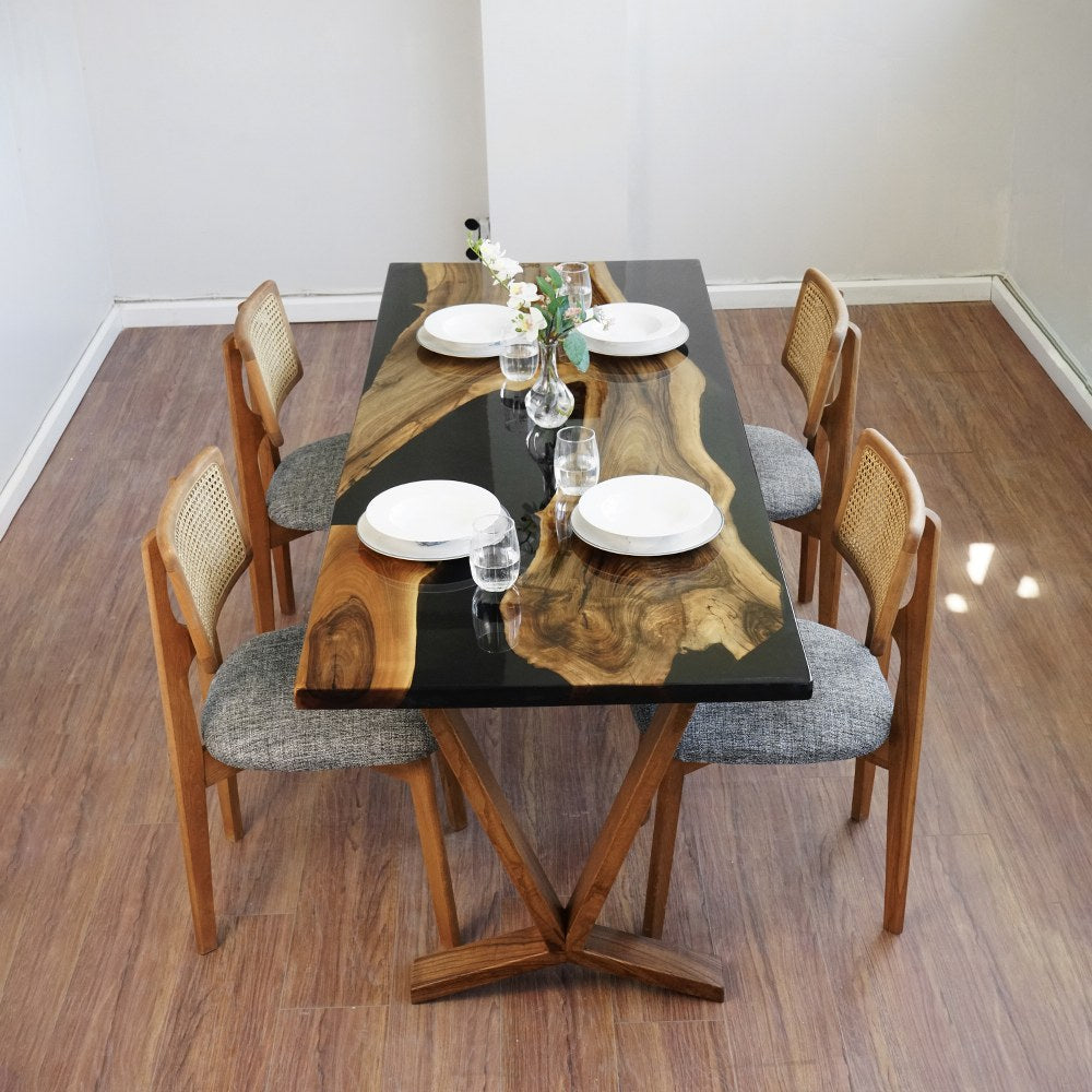 Front view of the live edge black walnut dining table with a black epoxy river, set for four with rattan back chairs