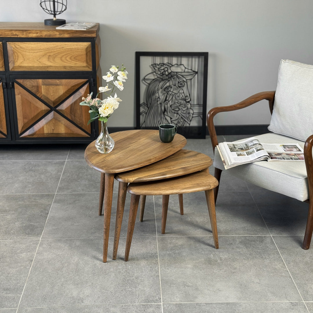 Three solid walnut pebble style nesting tables stacked together in front of a sideboard and armchair