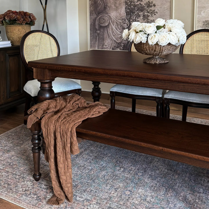 French country oak dining table with baluster legs, styled with cane back chairs and a matching bench in a formal dining room.