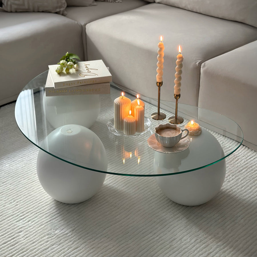 Bean shaped glass top coffee table on white wooden ball legs in front of a beige sectional sofa