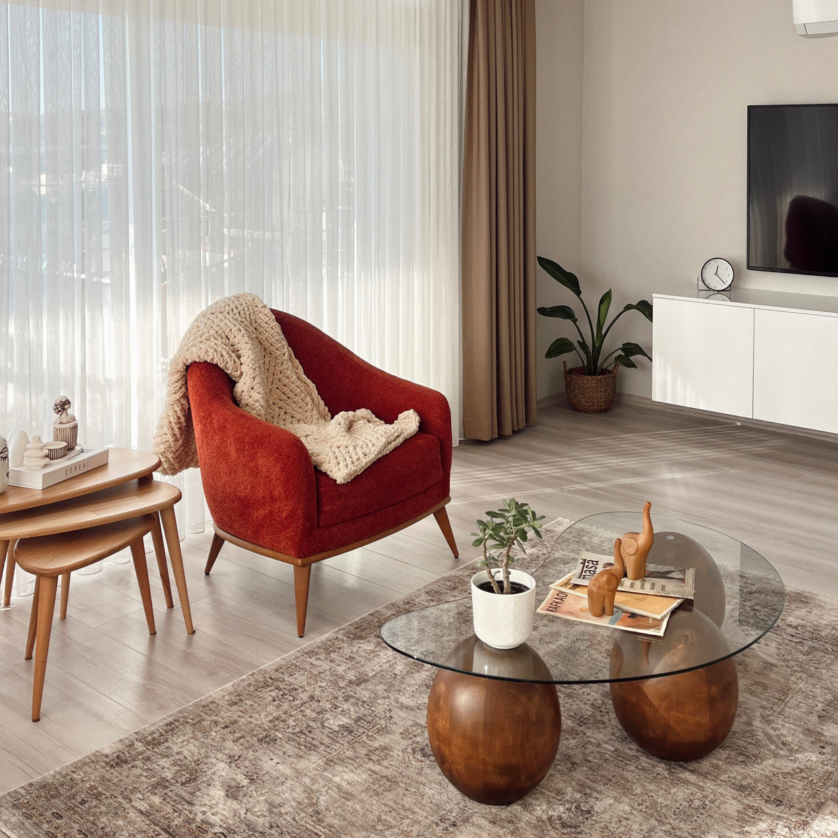 Wide room view of the glass coffee table with wooden ball legs, red armchair and nesting tables behind