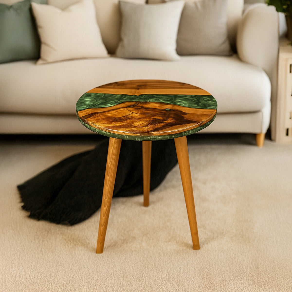 Green epoxy river round side table with a walnut top and three tapered legs in front of a sofa