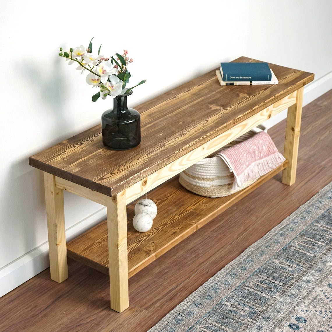 Entryway bench with a lower shoe shelf, angled from above with a basket, a folded towel and a book