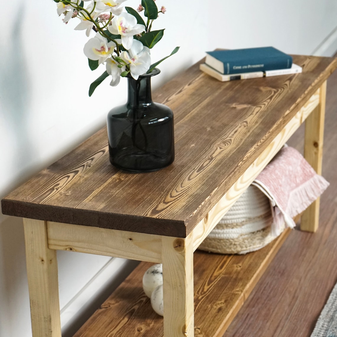 Close-up from above of the entryway bench top grain with a vase and a book, shelf and towel below