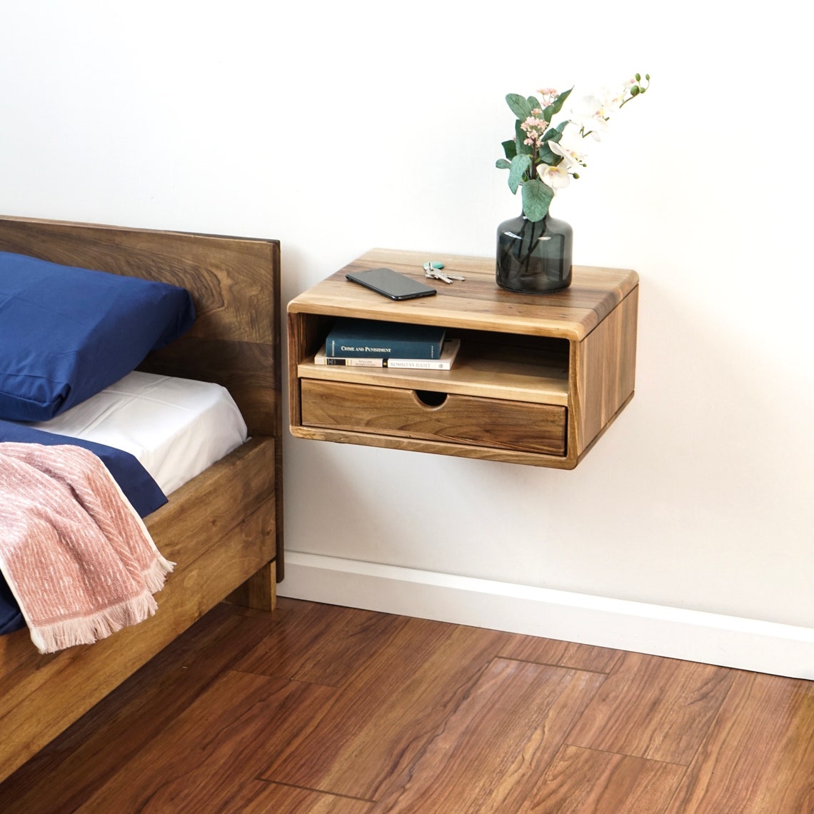 Walnut floating nightstand with open shelf and drawer, tight crop with the blue pillow at left