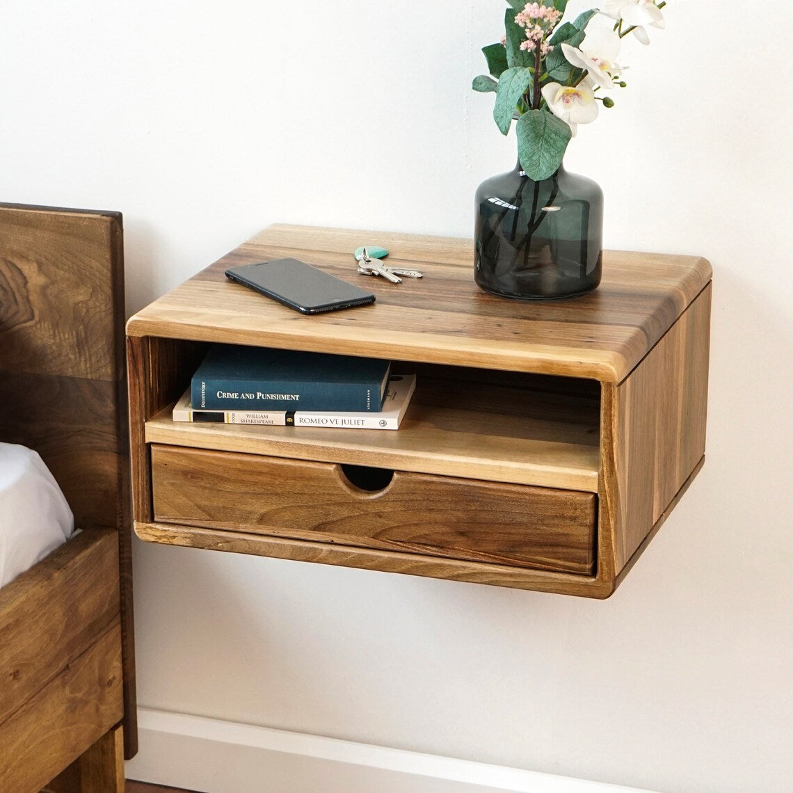 Walnut floating nightstand with open shelf and drawer beside a wood bed, angled view from above