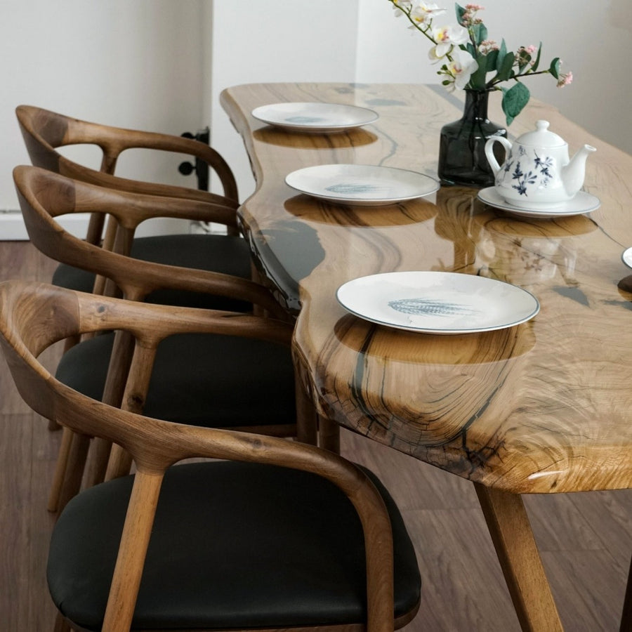 Close-up of the chestnut live edge farmhouse table with epoxy resin, set with plates and brown chairs