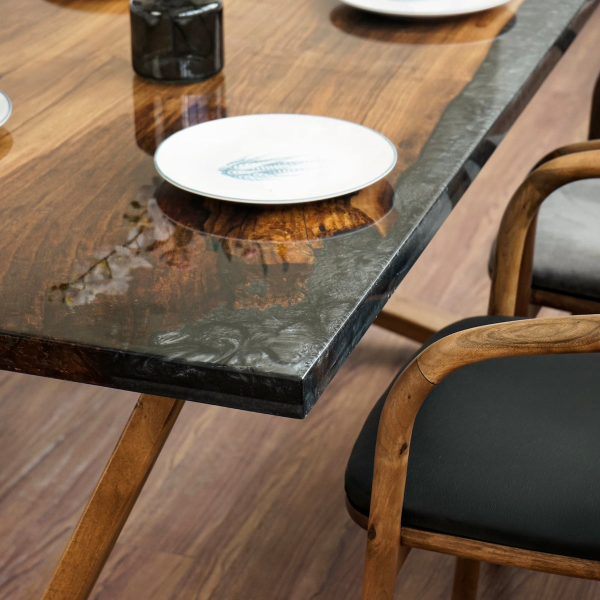 Close-up of the dark epoxy edge and walnut grain at the dining table corner, with a plate and a chair arm