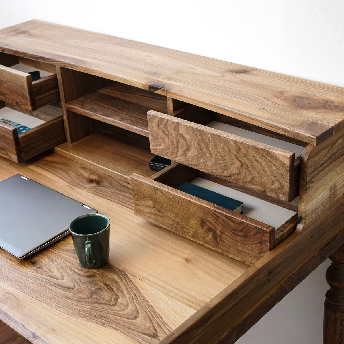 Close-up of open hutch drawers and the open shelf on the walnut desk, with walnut grain on the top