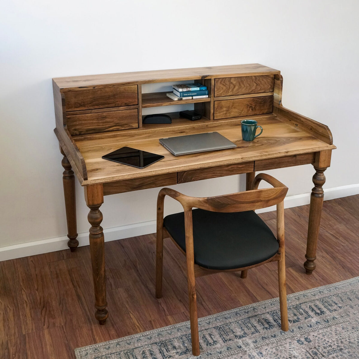 Three-quarter view of the walnut desk with hutch drawers, a laptop and a green mug on the desktop