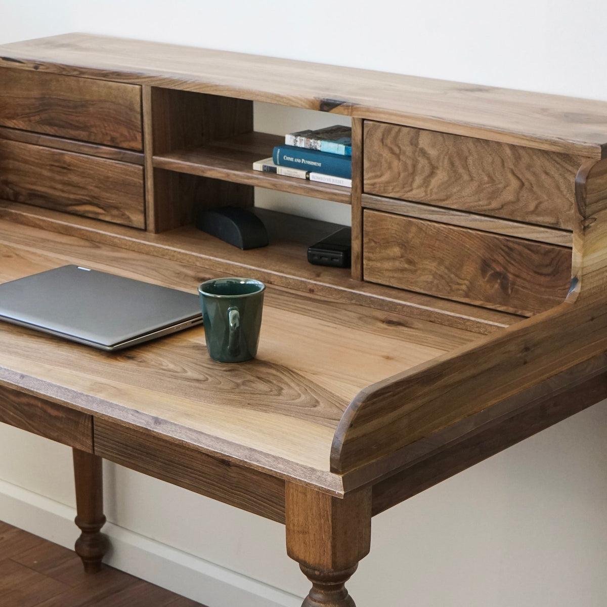 Hutch drawers and shelf of the walnut desk with a laptop and green mug on the desktop, from the left
