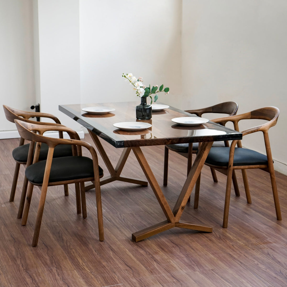 Walnut epoxy dining table from the far corner with armchairs on the near side and a vase of flowers