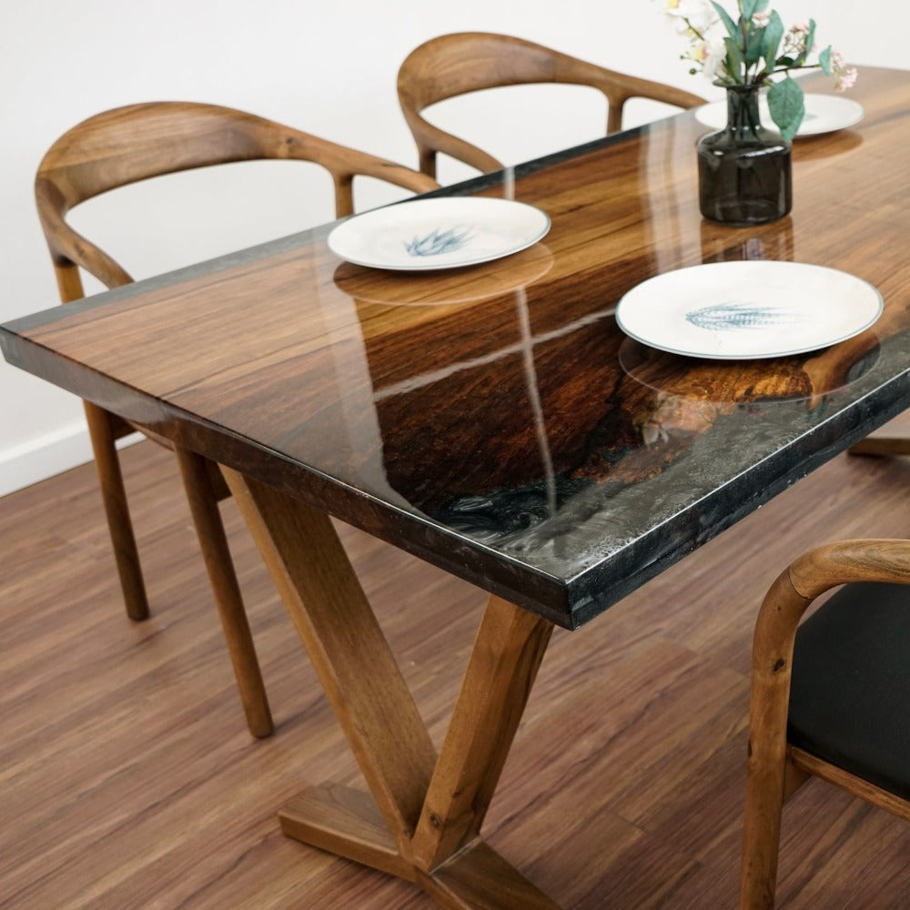 Close-up of the walnut tabletop corner with a glossy dark epoxy edge, a V shaped leg and a plate