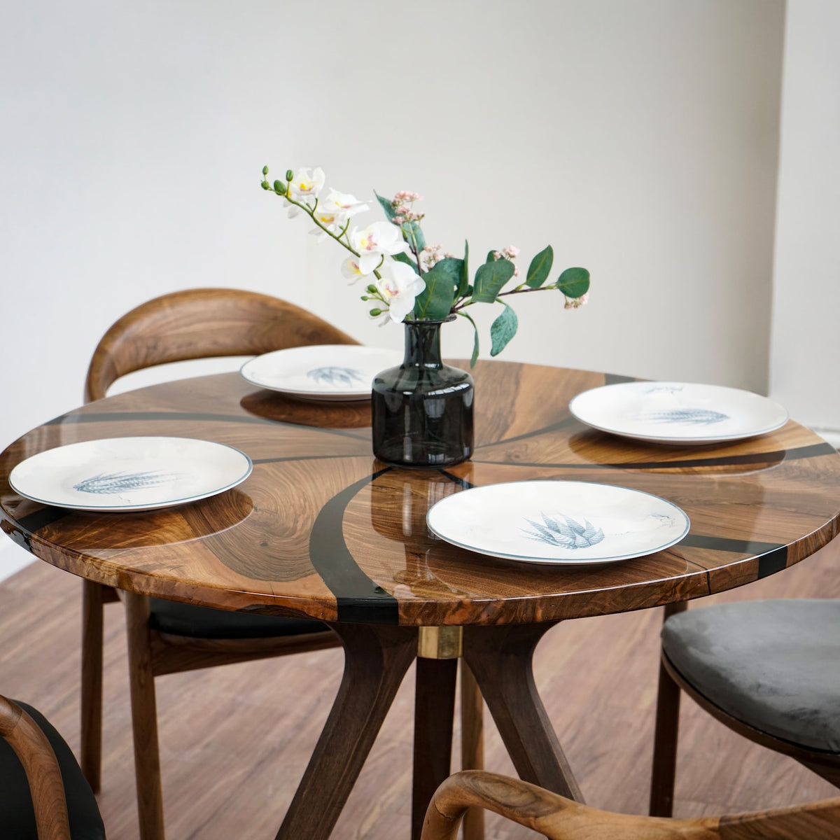 Close-up of the round walnut dining table top with black epoxy swirl and two place settings, wooden leg below
