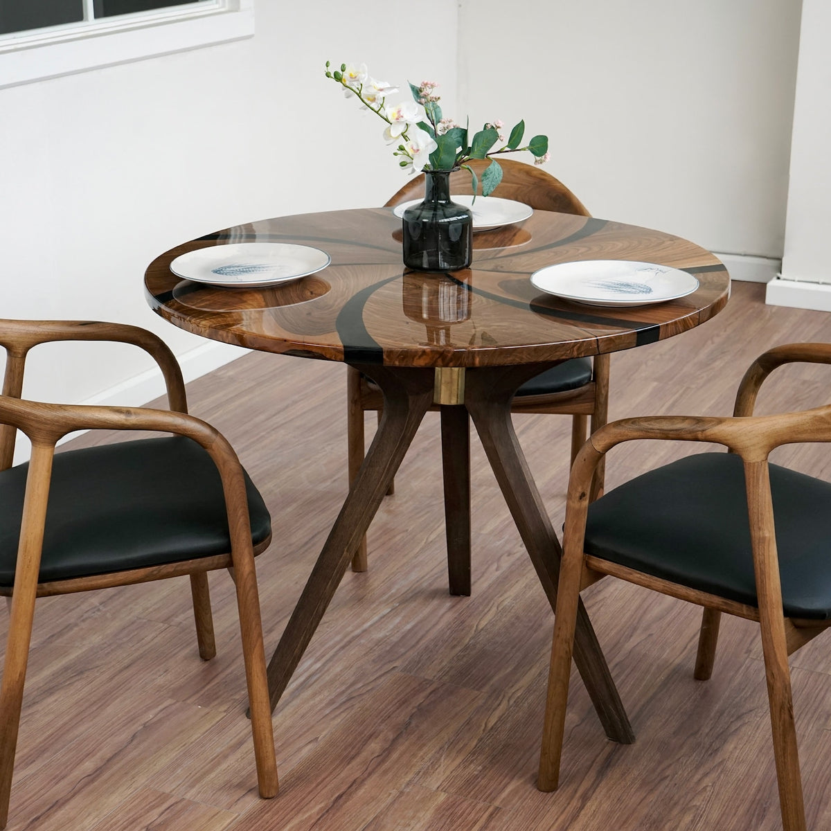 Round walnut dining table with epoxy swirl on wooden tripod legs, with two armchairs in the foreground