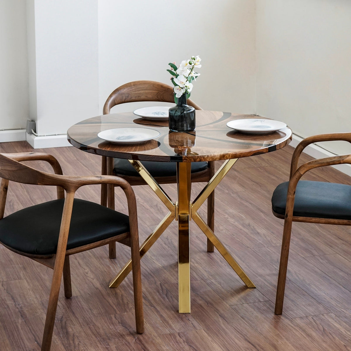 Round walnut dining table with epoxy top on gold crossed legs, front view with wooden armchairs