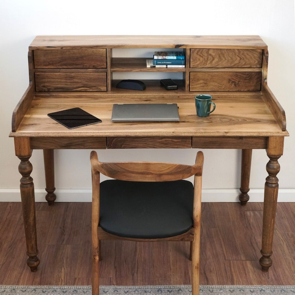Front view of the walnut desk with a four-drawer hutch, an open shelf and turned legs, a laptop on top